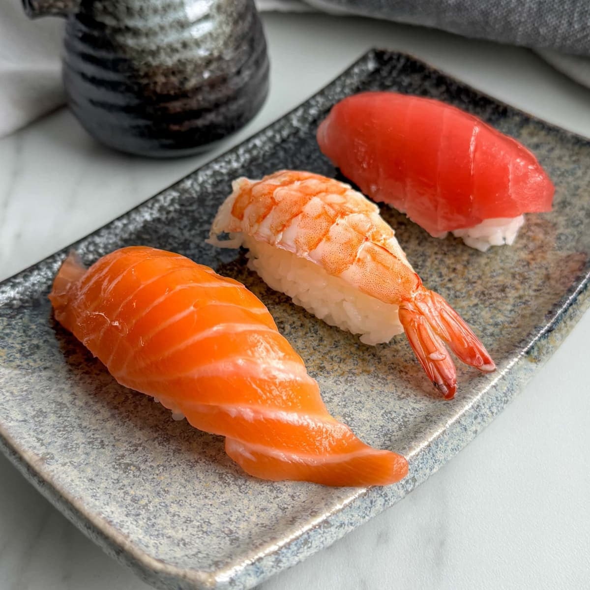Three pieces of nigiri sushi — salmon, prawn, and tuna — on a Japanese ceramic plate