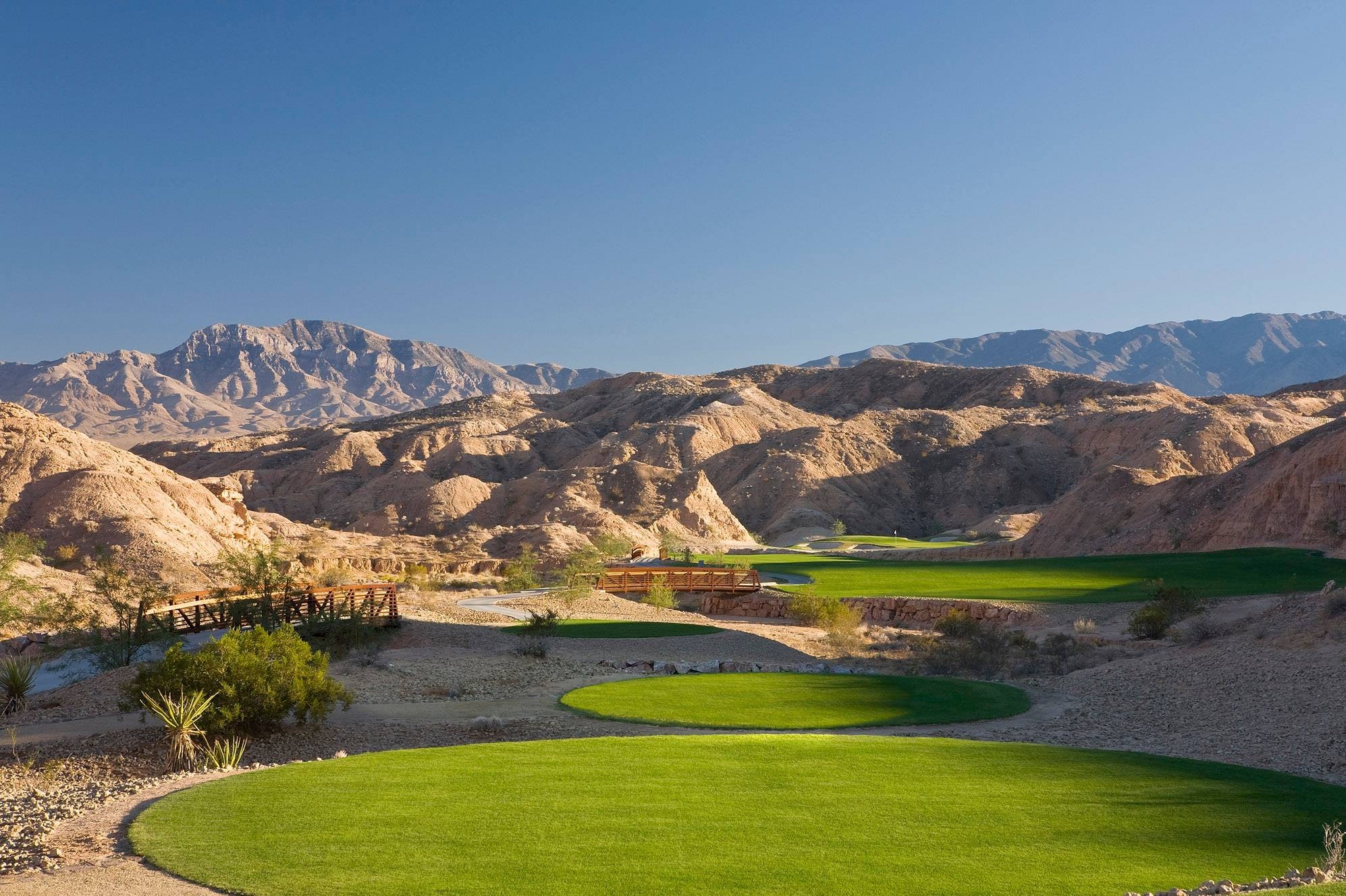 Conestoga Golf Club — green putting surface and wooden footbridge set against rugged Nevada desert mountains