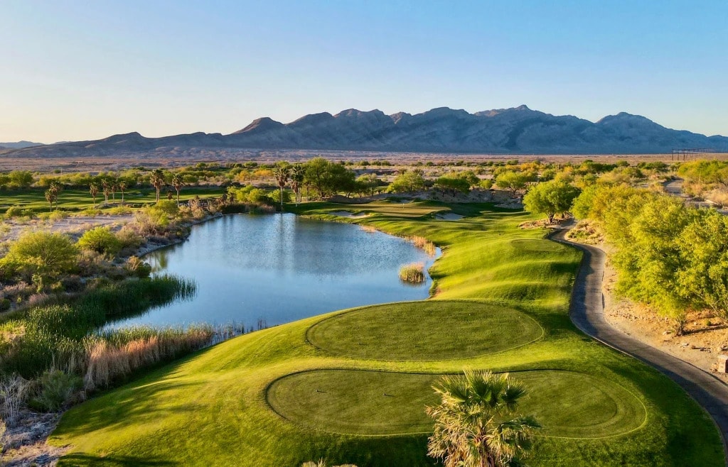 Coyote Springs Golf Club — desert fairway curving around a shimmering lake with mountain backdrop at golden hour
