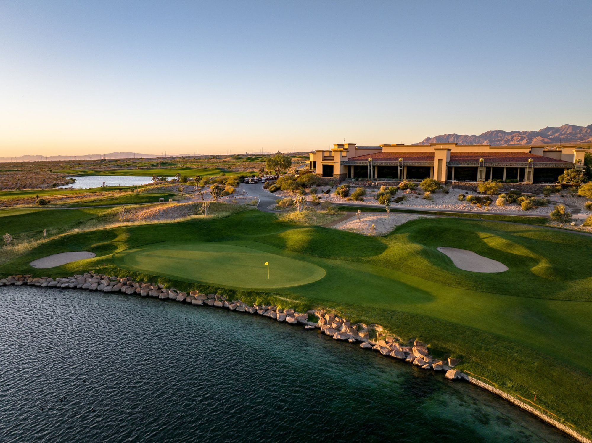 Las Vegas Paiute Golf Resort at sunset — island-style green beside a lake with the adobe-style clubhouse behind